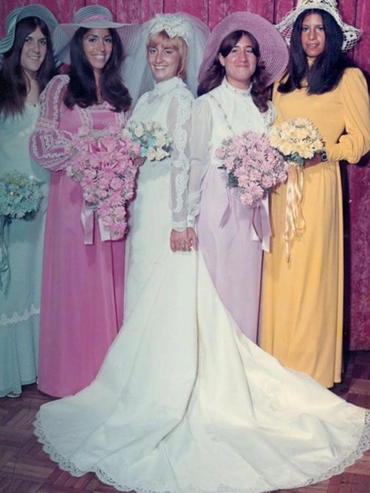 1978 Wedding Dresses and 4 Timeless Styles to Know 2 A bride in a white lace dress stands with four bridesmaids in colorful dresses and large hats.