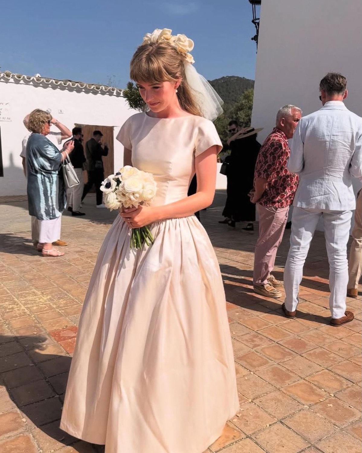 1978 Wedding Dresses and 4 Timeless Styles to Know 3 A bride in a cream satin wedding dress holding a white rose bouquet outdoors.