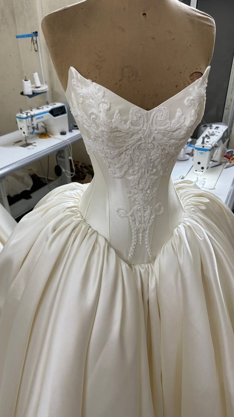 White satin wedding dress with intricate bespoke embroidery on the bodice displayed on a mannequin.