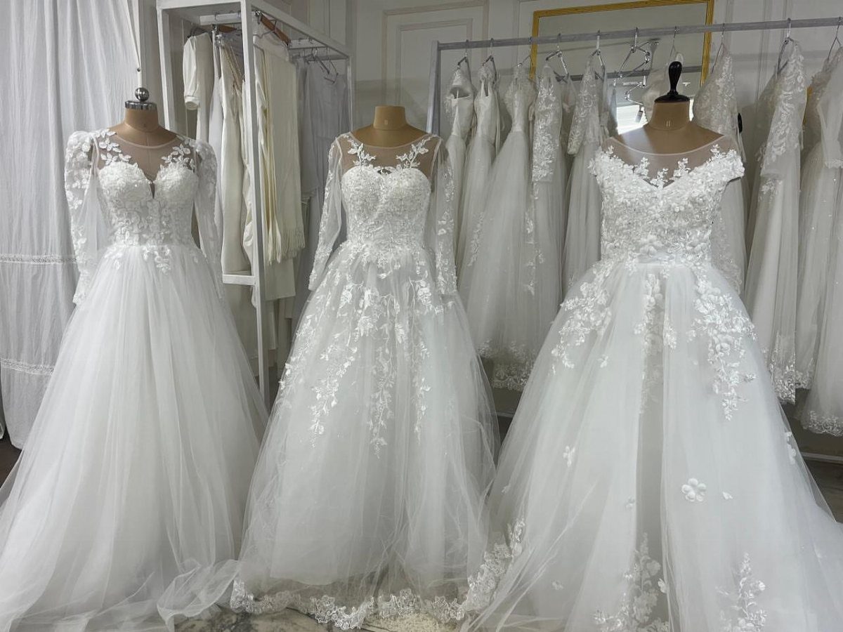 Three white lace wedding dresses displayed on mannequins inside a bridal boutique.