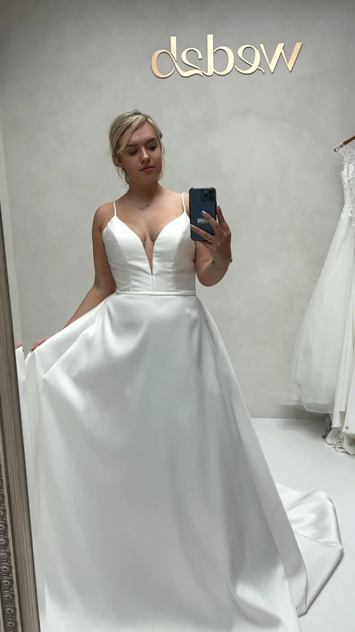 A woman in a white V-neck A-line wedding dress taking a mirror selfie.