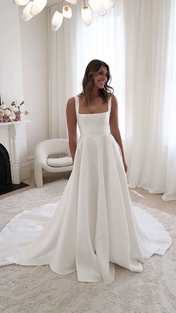 A smiling woman posing in a white satin wedding dress with a full skirt.