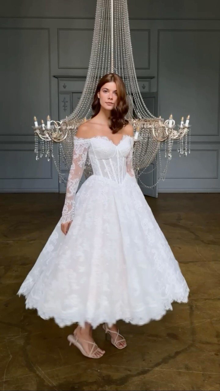 Woman wearing a white lace tea-length wedding dress with off-the-shoulder sleeves and a corset bodice.