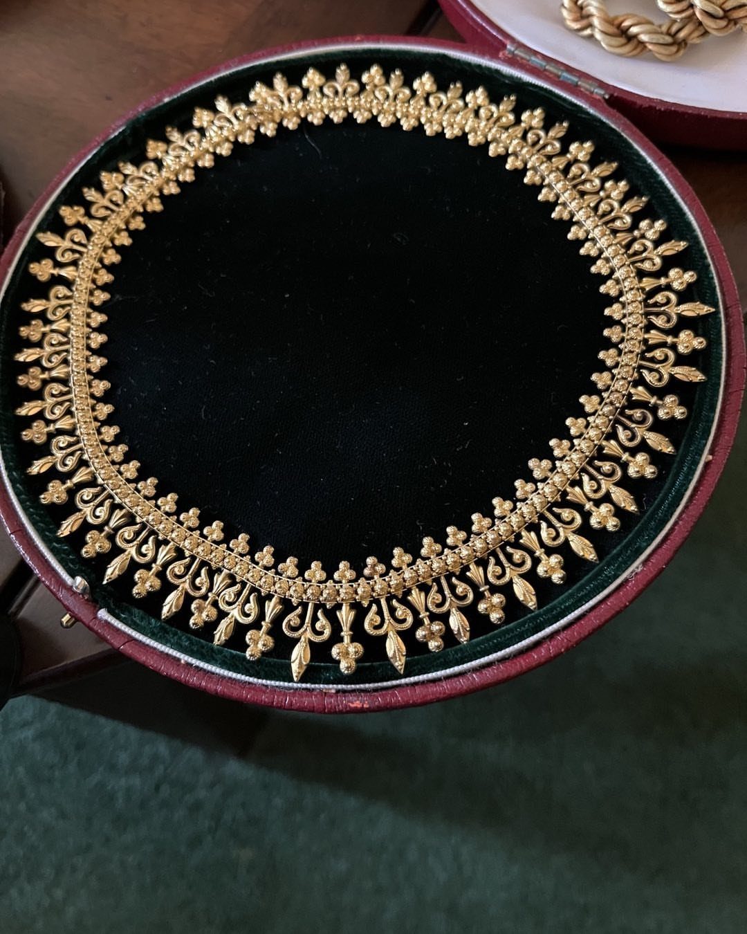 Gold filigree necklace resting on a dark green velvet cushion inside a red jewelry box.