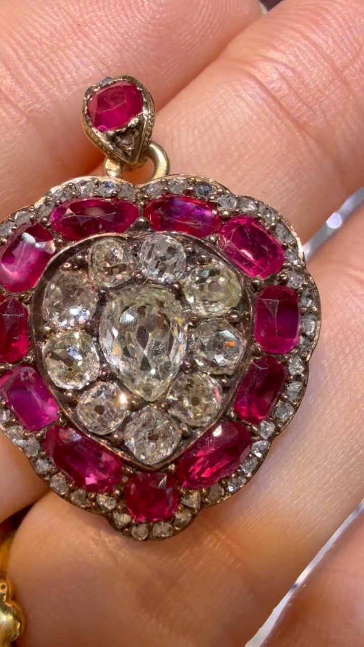 A gold pendant with a large pear-shaped diamond and ruby border held between two fingers.