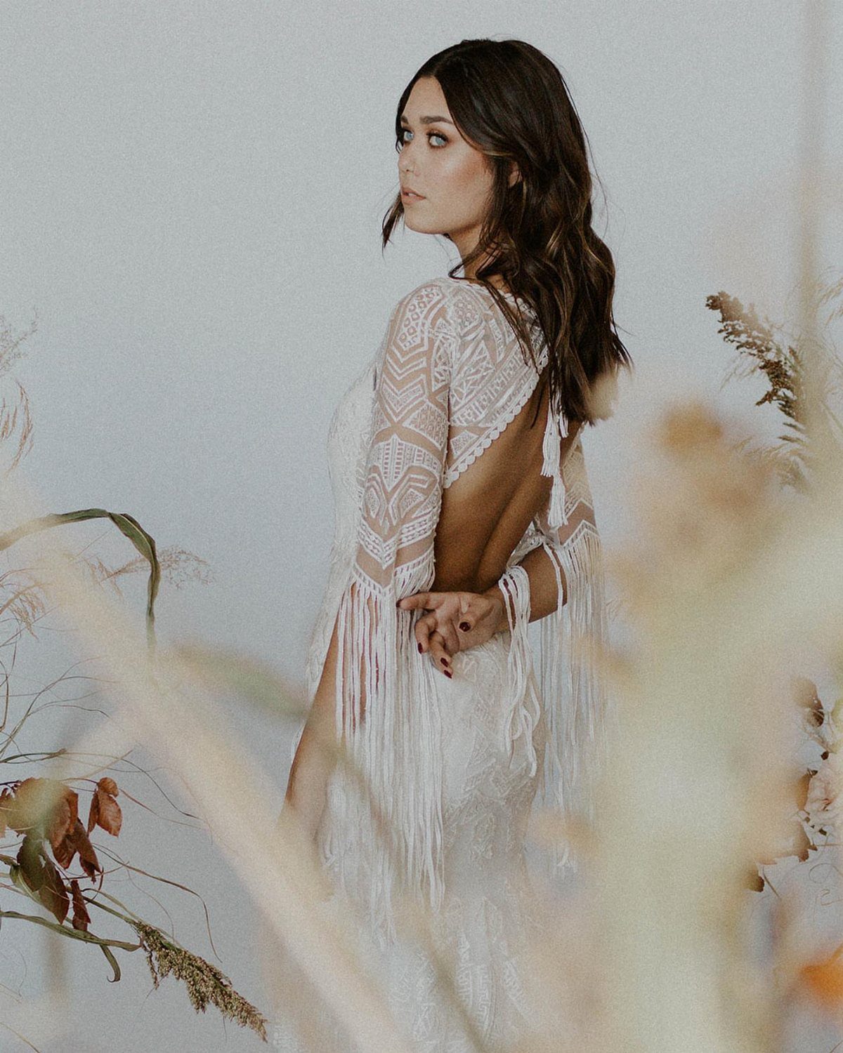 Art Deco Wedding Dress: 11 Styles From Beaded Trains to Choker Accents 6 Woman wearing a white lace wedding dress featuring long decorative fringe on the sleeves.