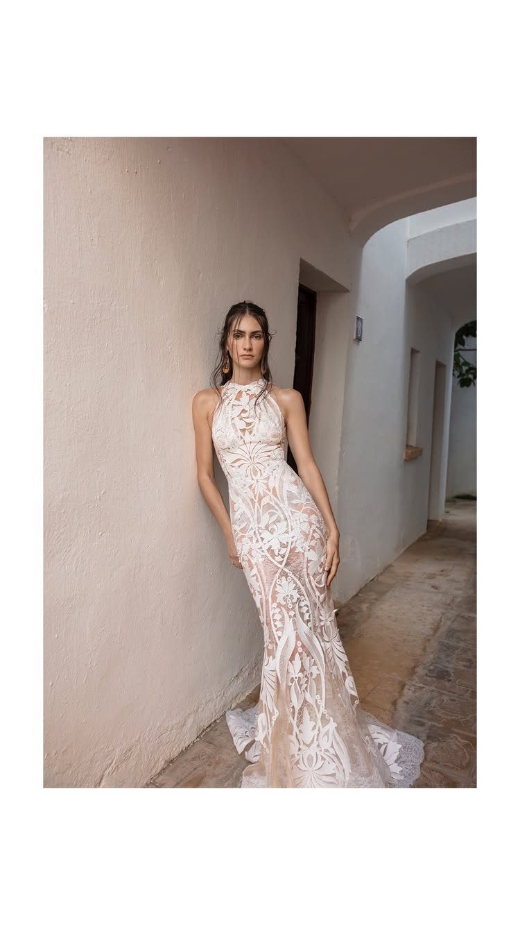 Art Deco Wedding Dress: 11 Styles From Beaded Trains to Choker Accents 4 Woman wearing a white halter-neck wedding dress with intricate geometric lace patterns standing in a corridor.