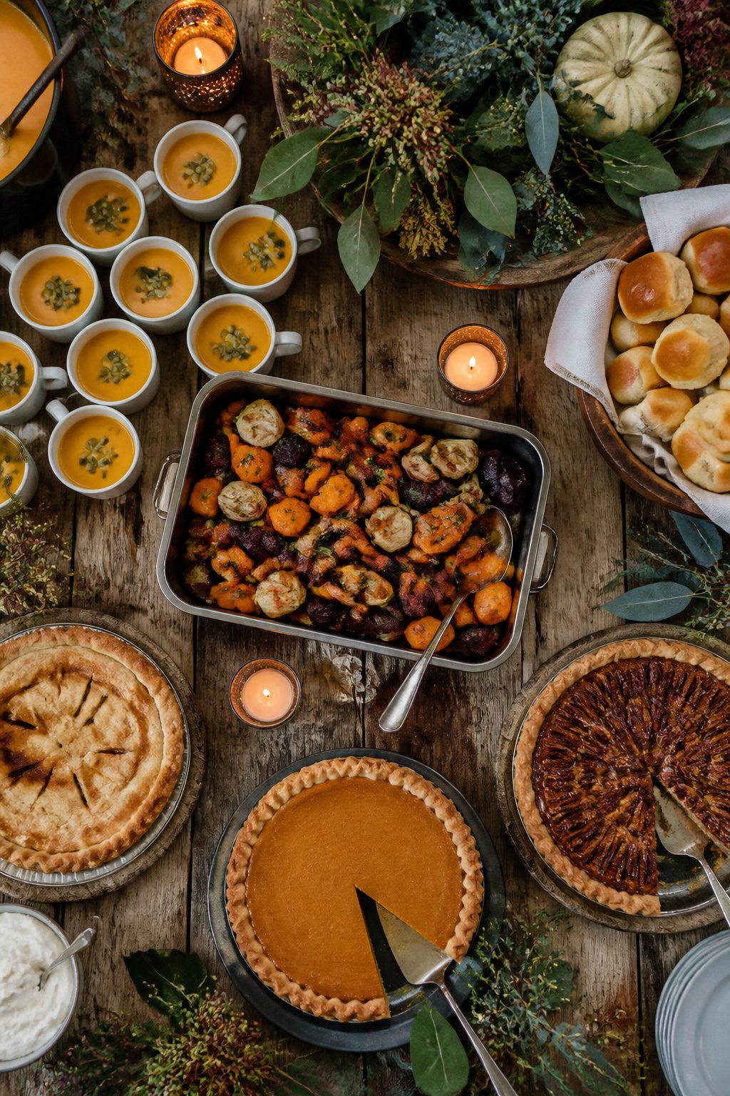 Small cups of pumpkin soup and colorful roasted root vegetables on a table.