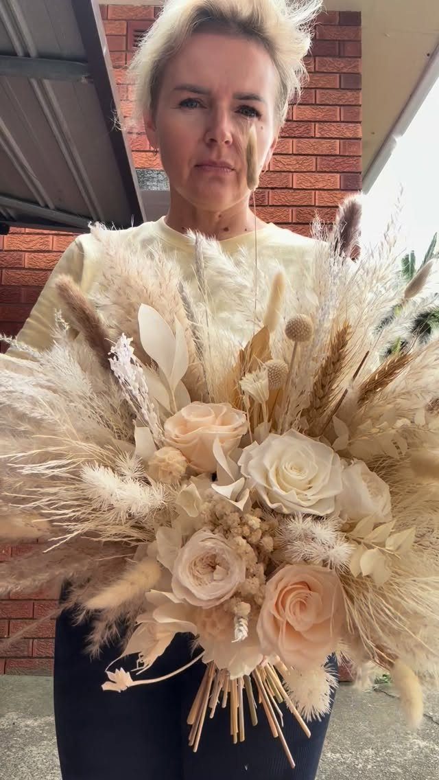 A woman holding a large boho wedding bouquet featuring dried pampas grass and cream roses.