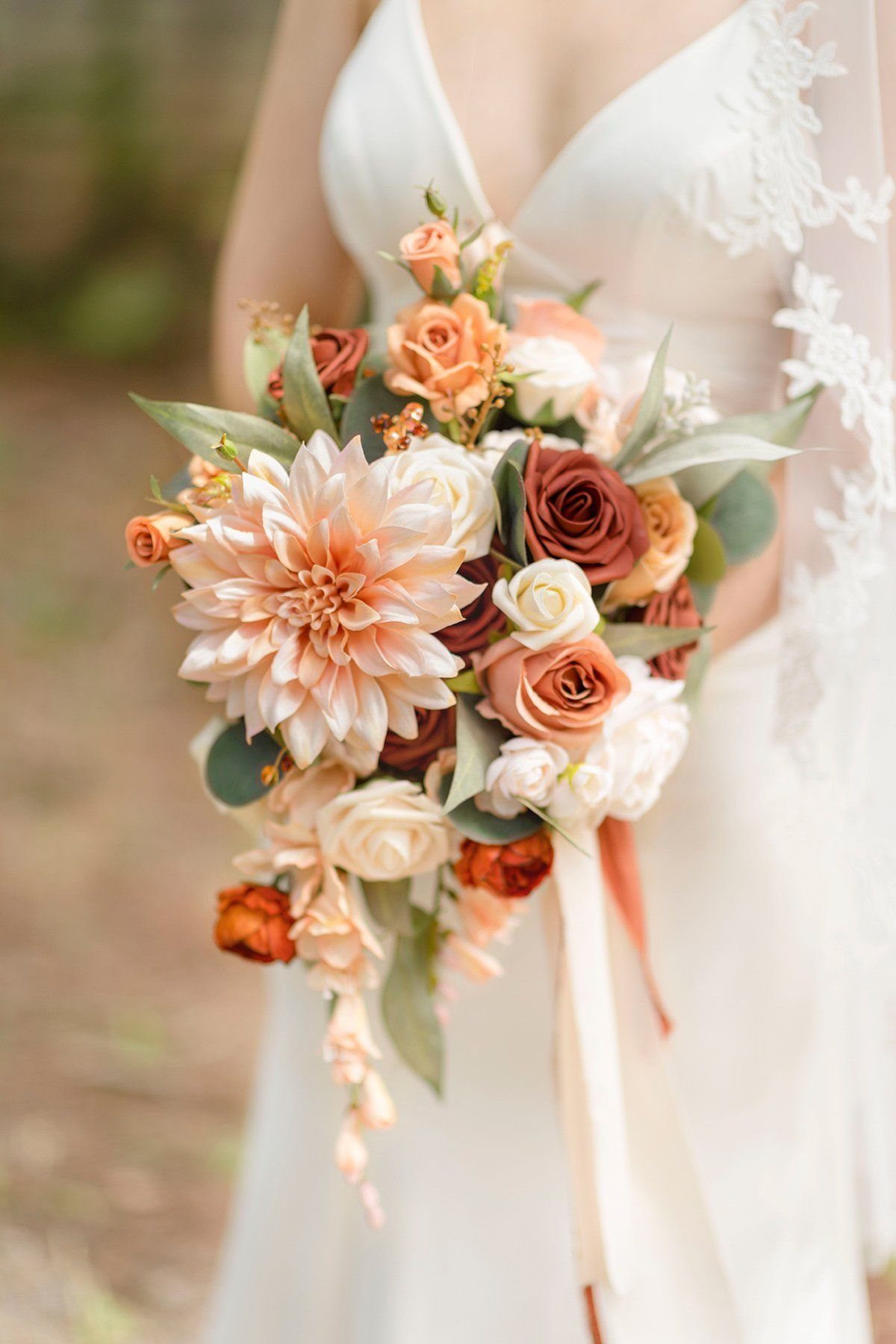 A bridal bouquet with peach dahlias and roses featuring long flowing silk ribbons hanging down.