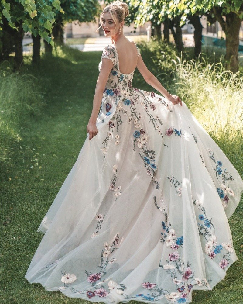 Woman in a white Regency-style gown with blue and purple floral embroidery standing in a garden.