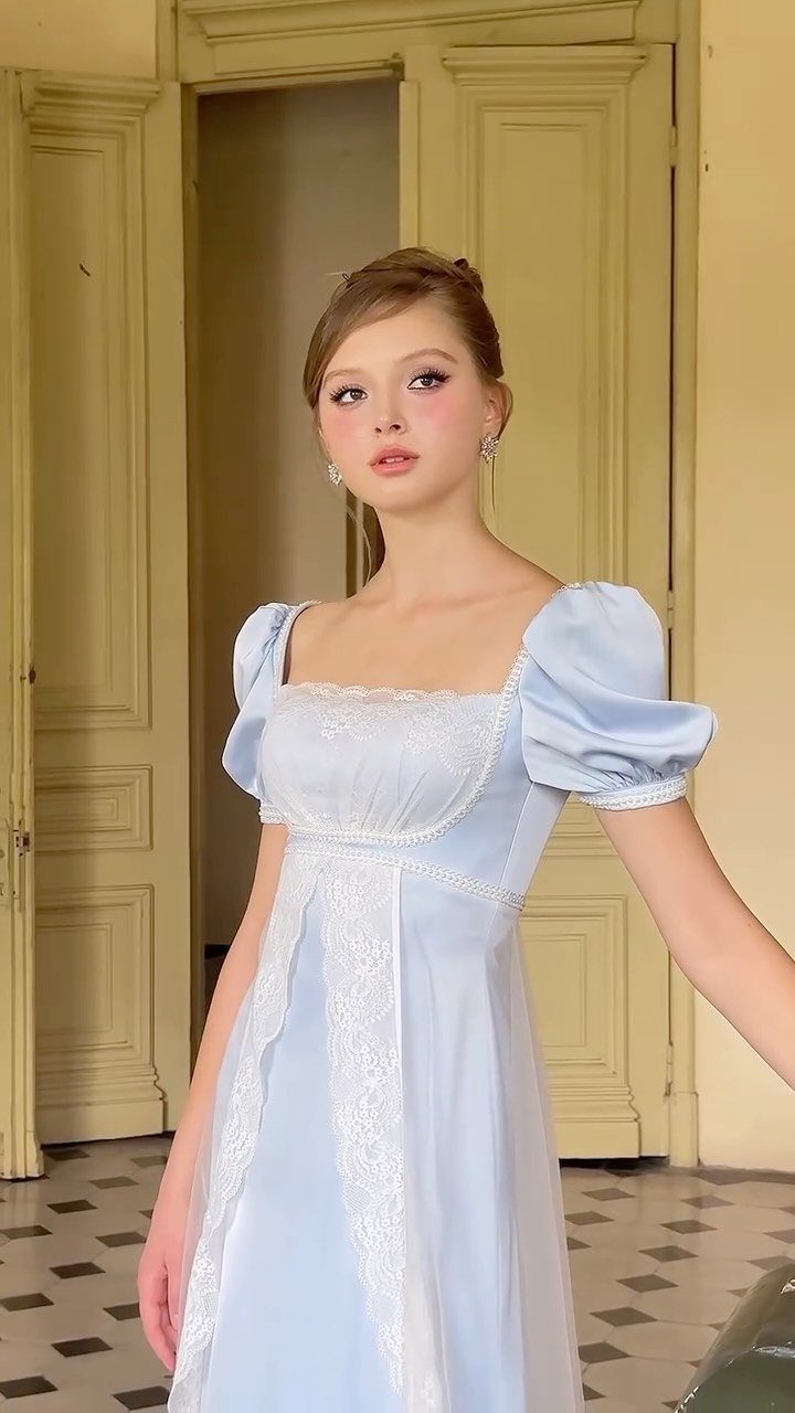 Young woman wearing a light blue empire waist gown with lace details and puffed sleeves.