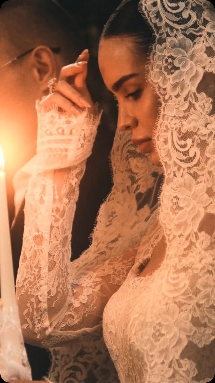 A woman wearing an intricate white lace wedding dress and a matching lace veil.
