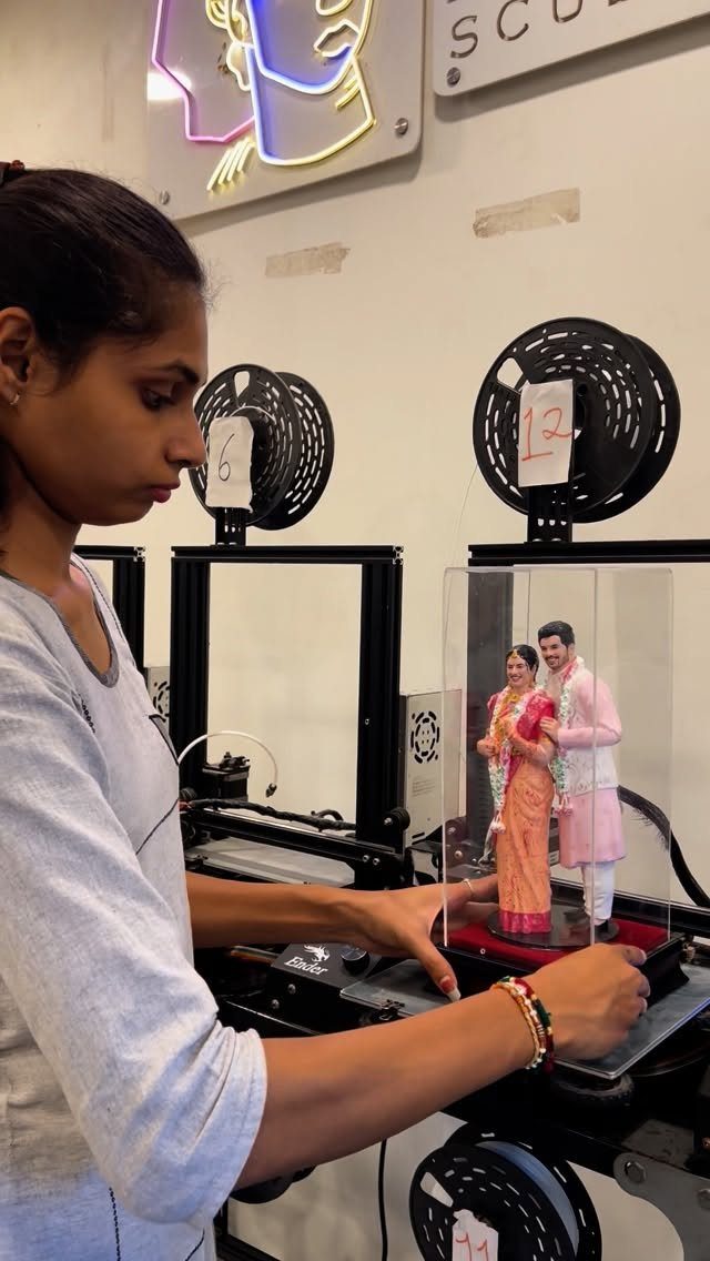 A woman adjusting a 3D-printed wedding couple figurine inside a clear display case.