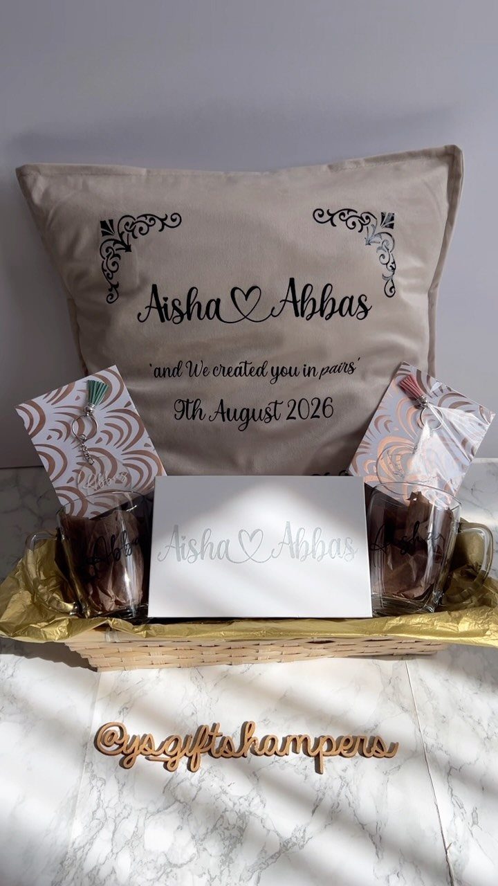 A gift hamper featuring a personalized beige cushion with names and a date.