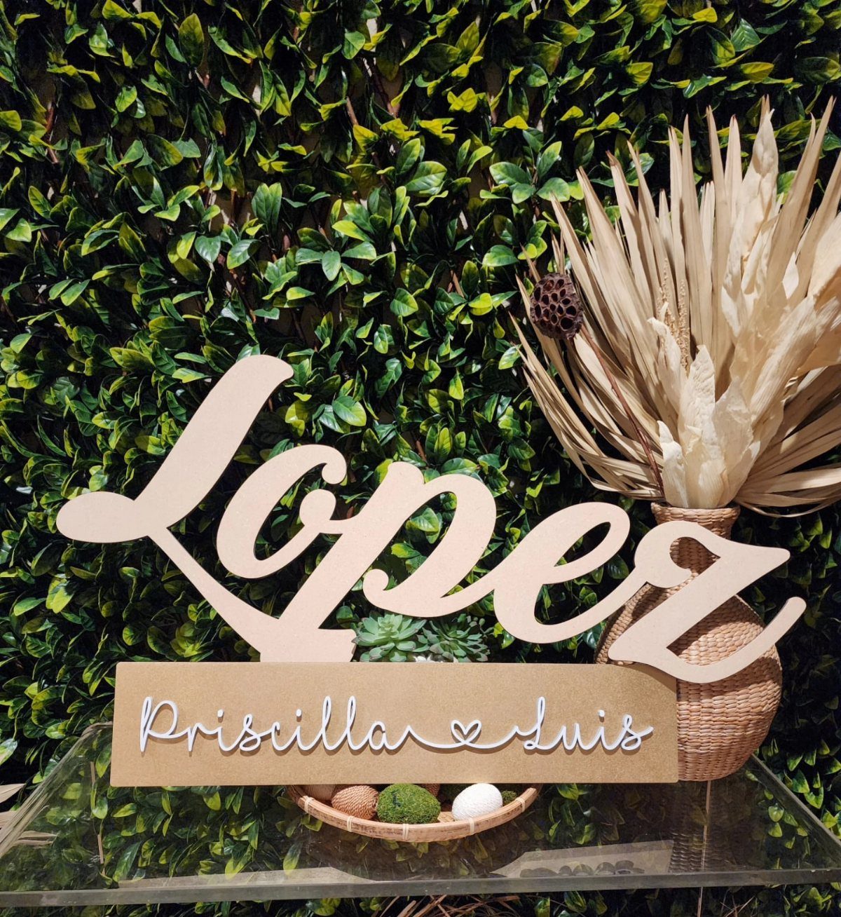 Wooden Lopez family name sign with Priscilla and Luis text against a green leaf background.