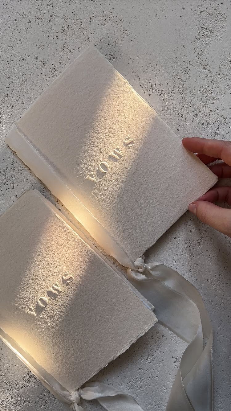 Two textured white vow books with embossed text resting on a grey surface.