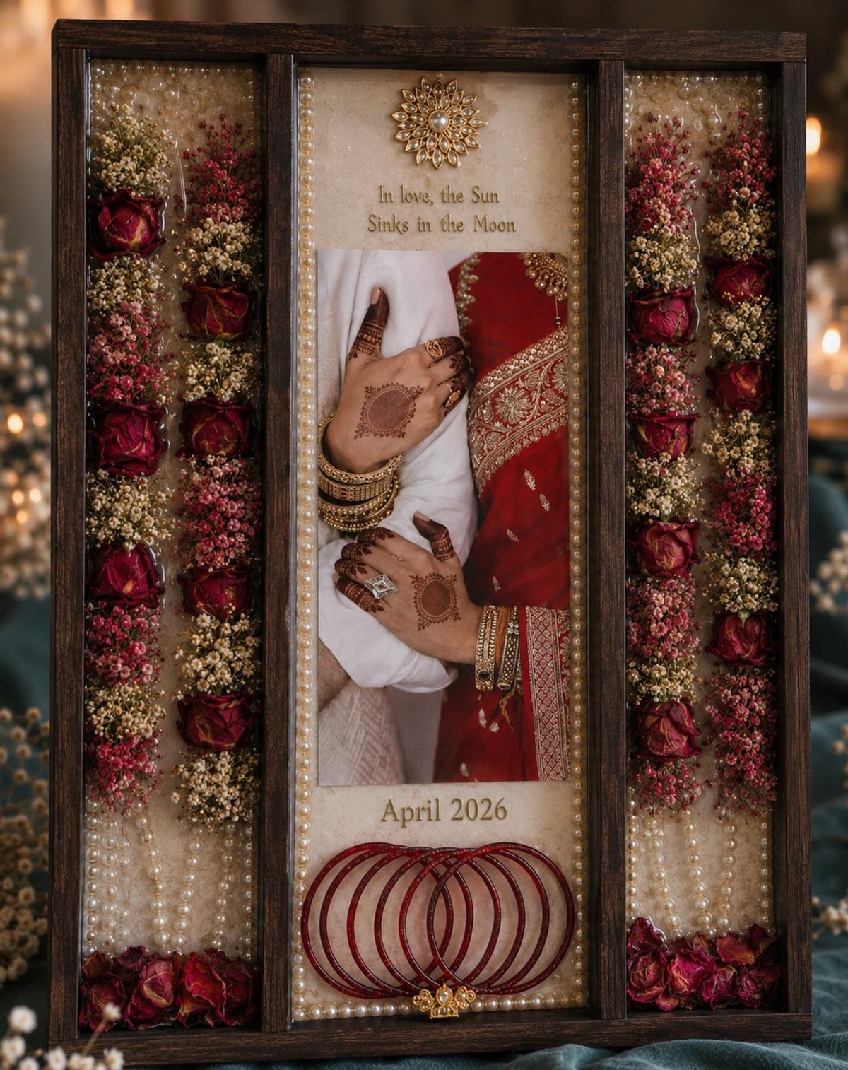 A wooden shadow box containing a wedding photo, dried roses, pearls, and red bangles.