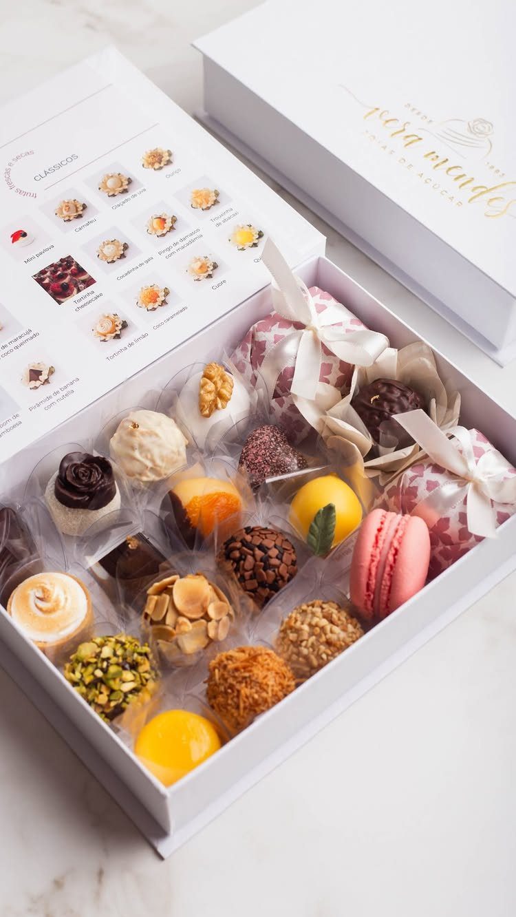 An open white gift box filled with assorted gourmet chocolates, colorful macarons, and truffles on marble.