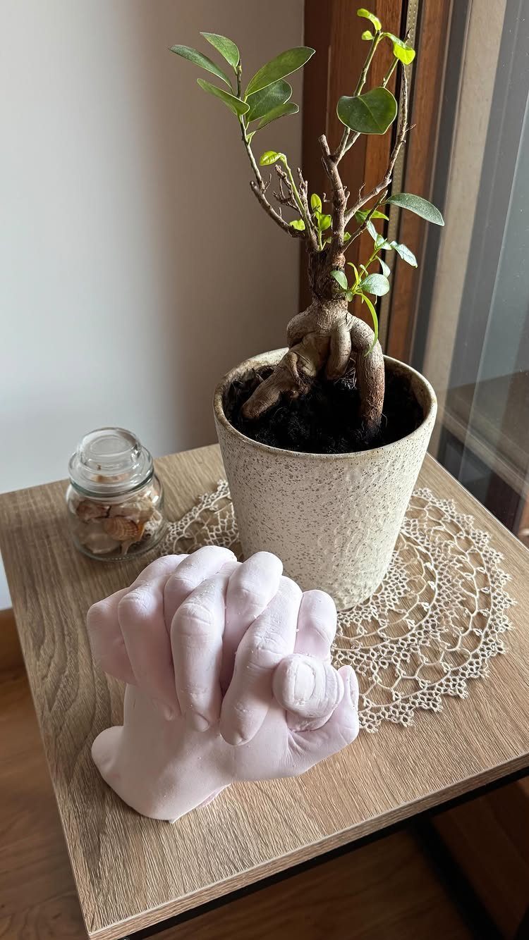 A pink hand casting sculpture of two interlocking hands sits on a wooden table.