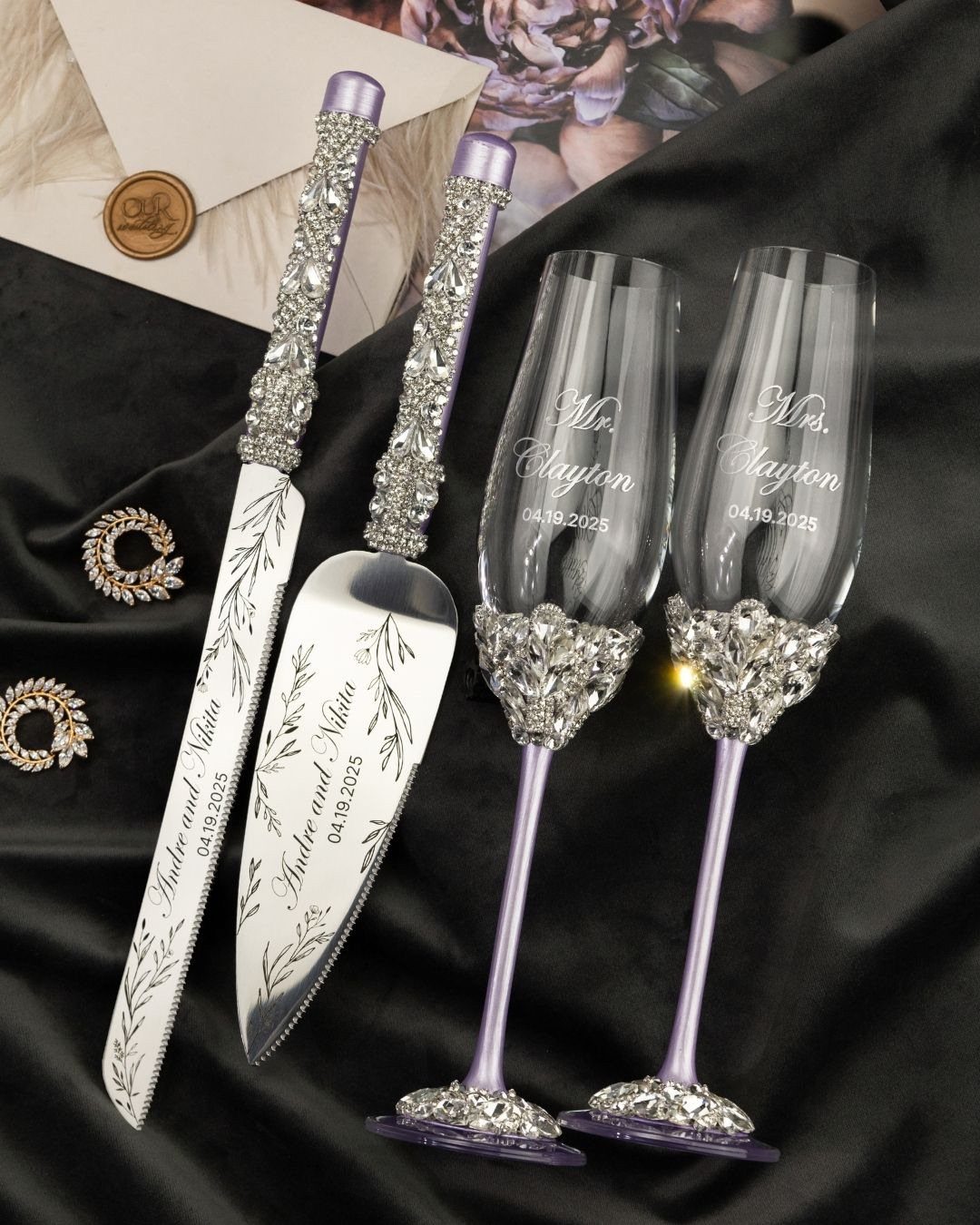 Personalized champagne flutes and silver cake serving set with crystal embellishments on black fabric.