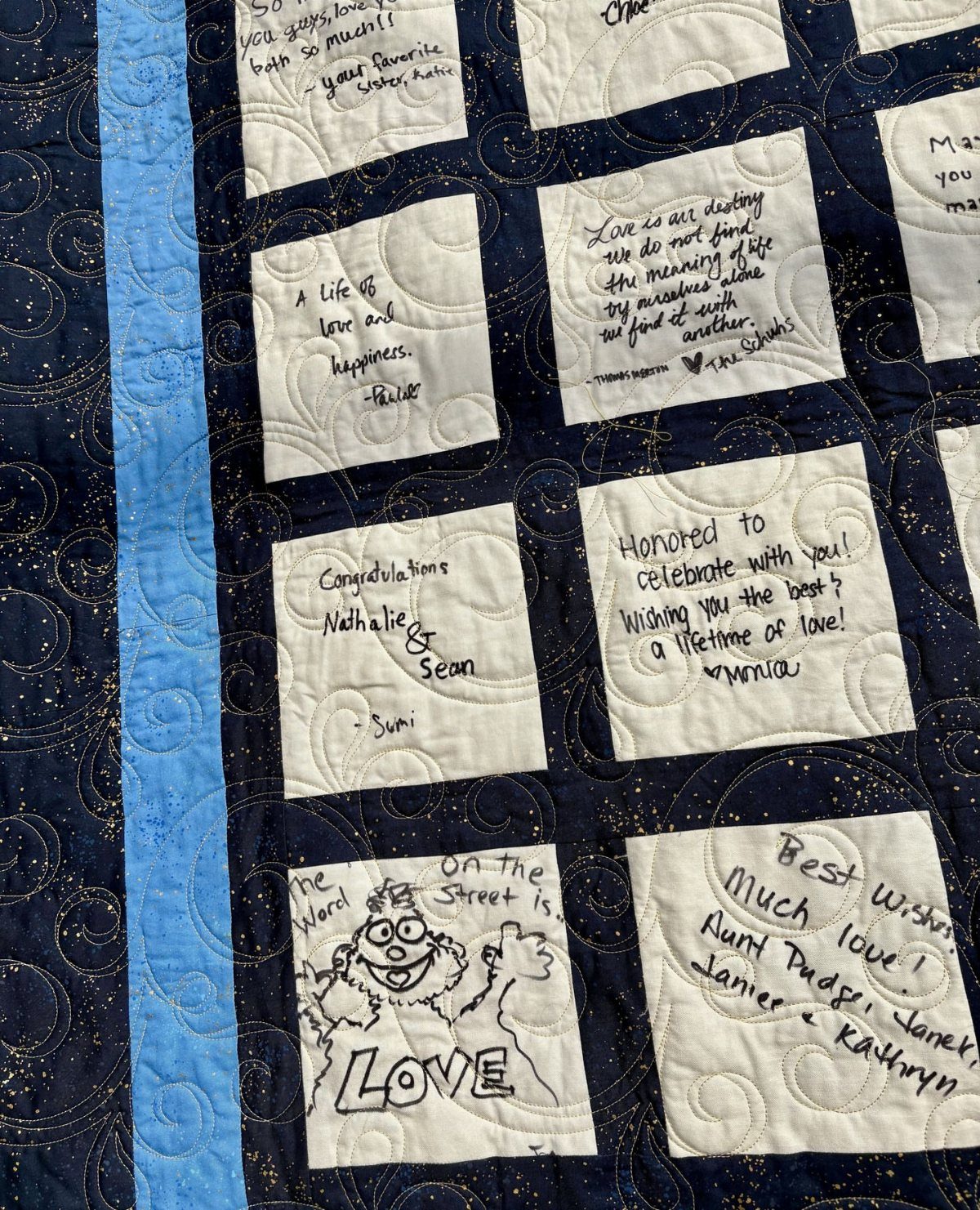 A navy blue quilted blanket with white squares containing various handwritten messages and drawings.