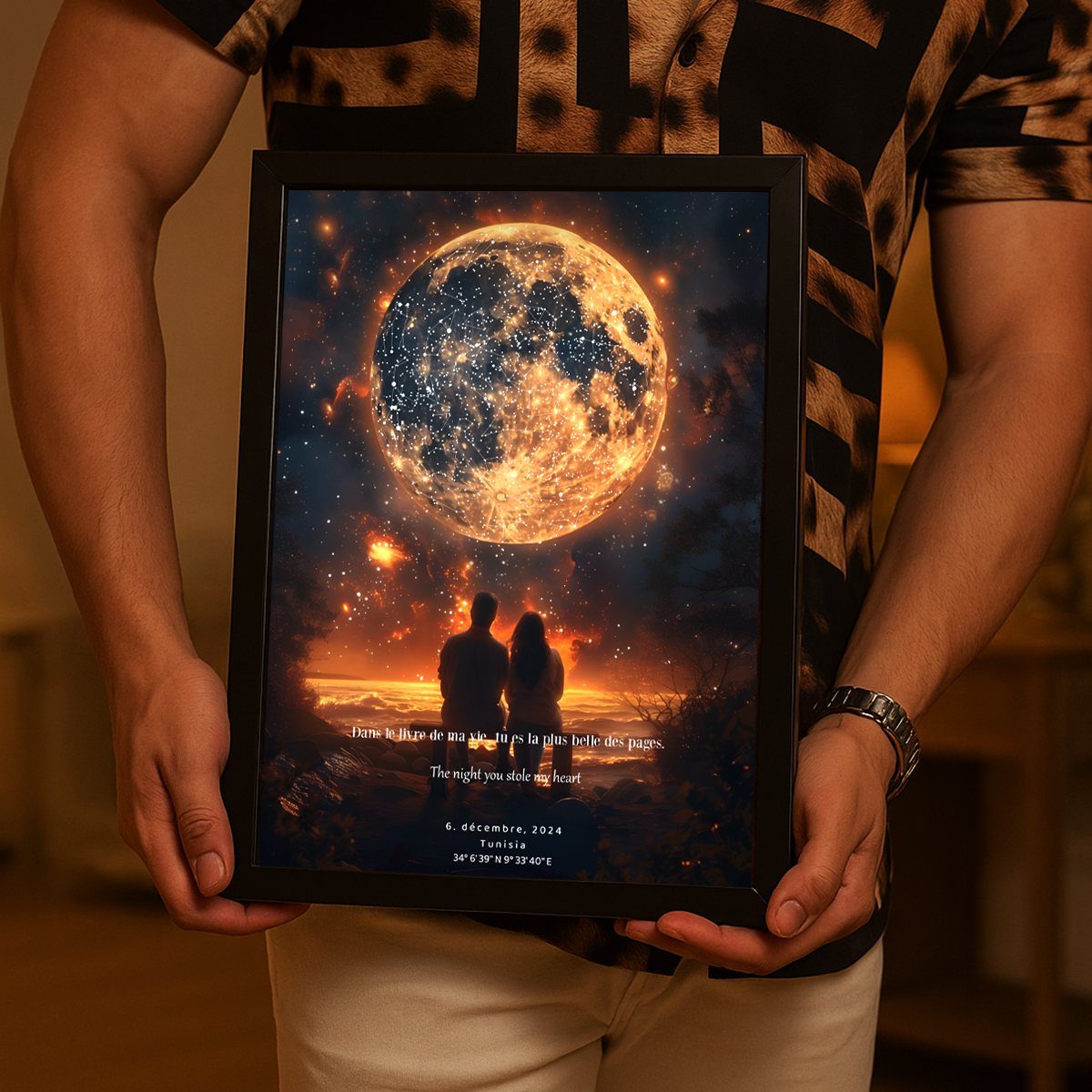 A person holding a framed personalized moon art print featuring a couple's silhouette by the sea.