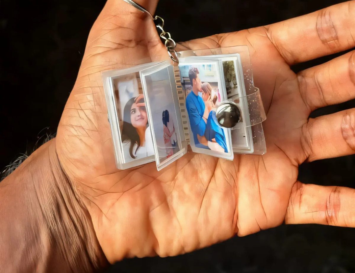 A hand holding a clear accordion keychain filled with small personalized photographs of a couple.