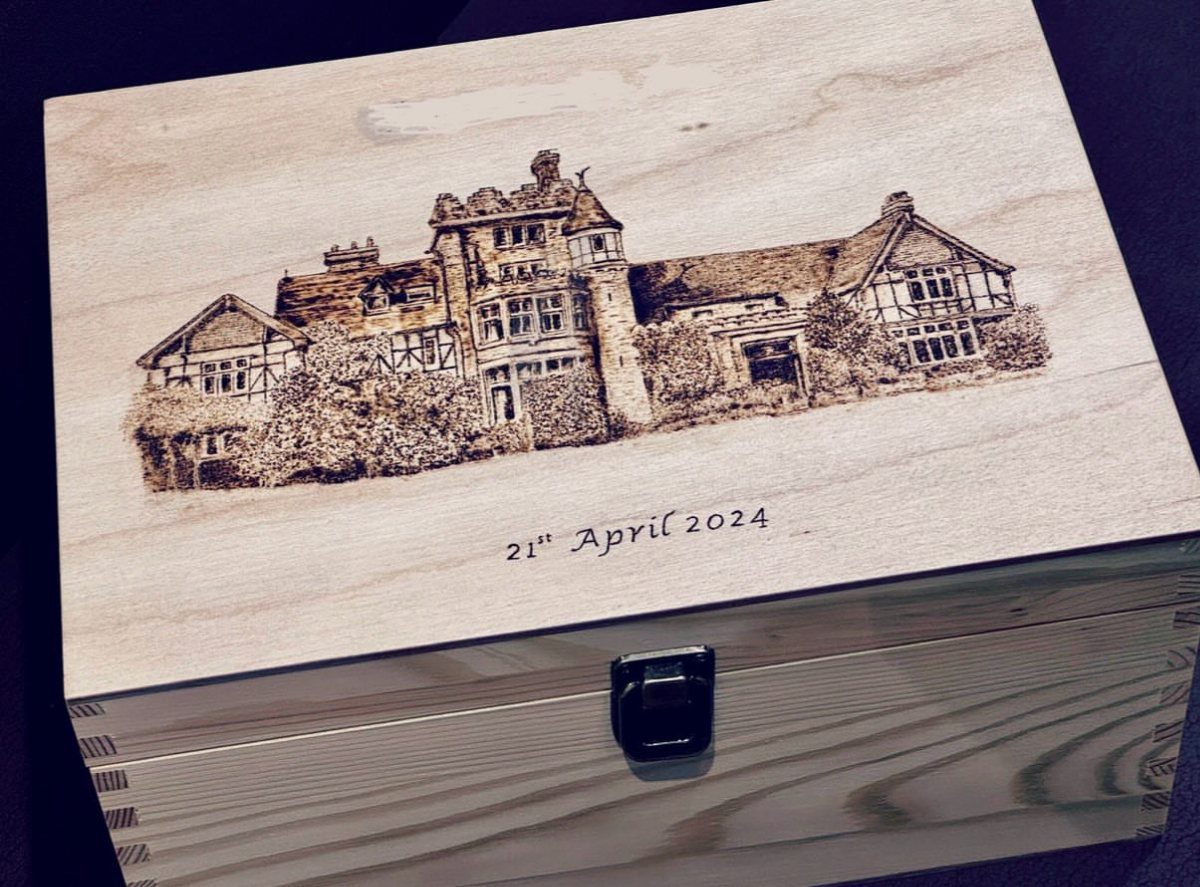 A wooden keepsake box with a burnt manor house illustration and a specific date.