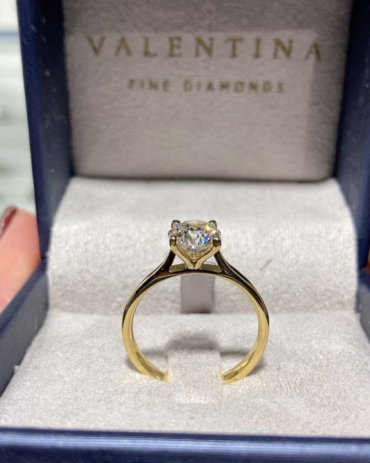 A gold solitaire diamond ring resting inside a blue velvet Valentina Fine Diamonds jewelry box.