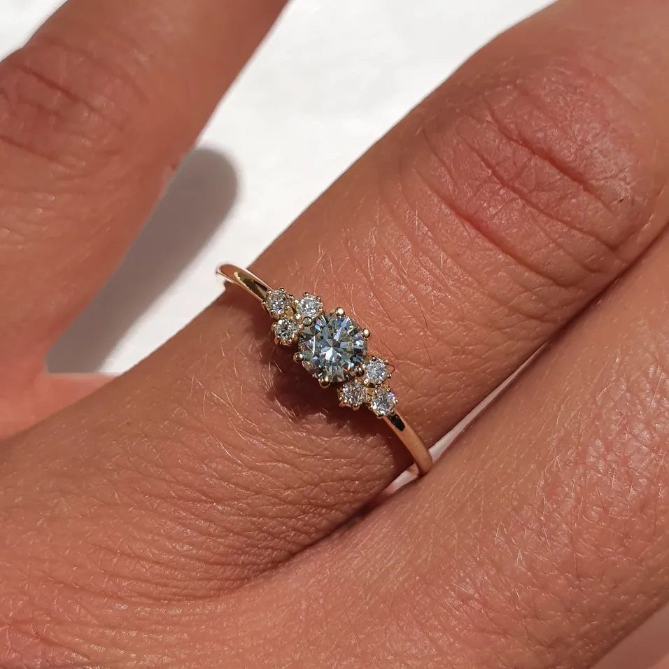 A rose gold ring with a cluster of five diamonds on a person's finger.
