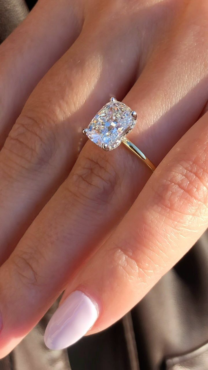 A cushion-cut diamond engagement ring on a thin gold band worn on a finger.