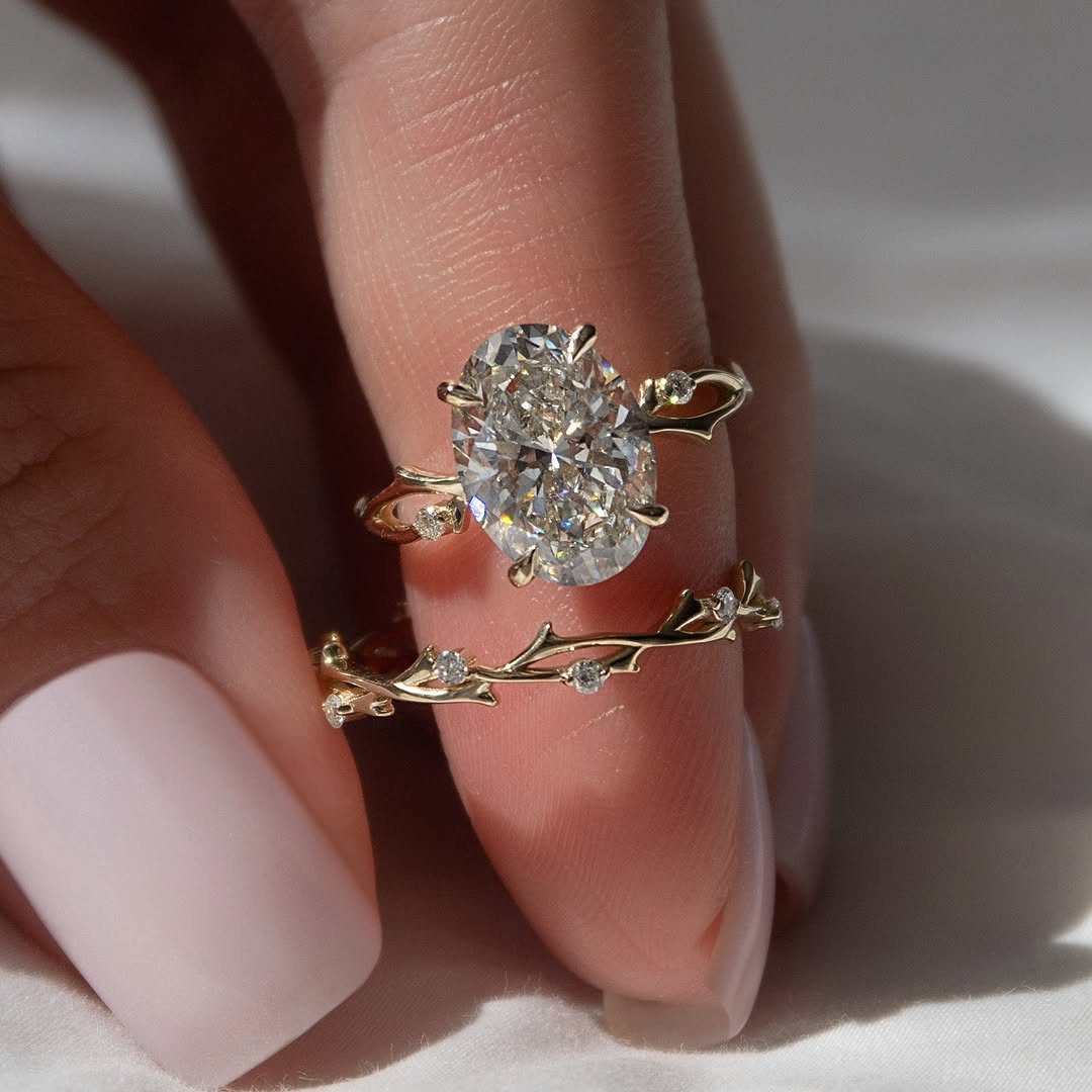 Two gold rings with oval diamonds and nature-inspired vine patterns worn on a finger.