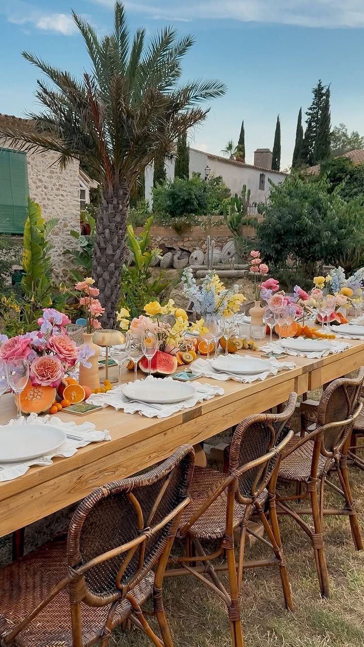A long wooden table set with colorful flowers and citrus for an outdoor Mediterranean wedding feast.