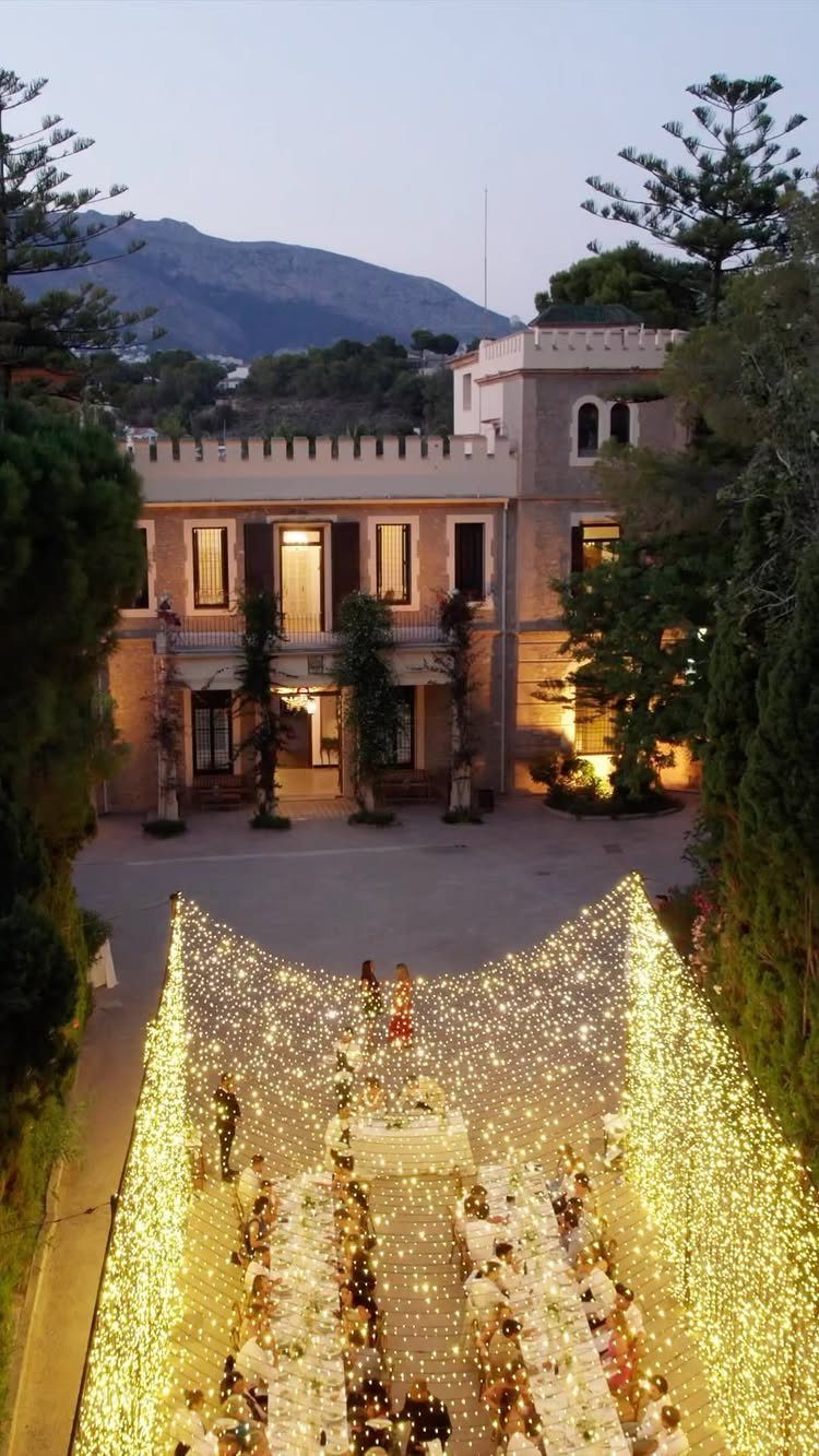 Aerial view of a wedding banquet under a canopy of fairy lights in a villa courtyard.