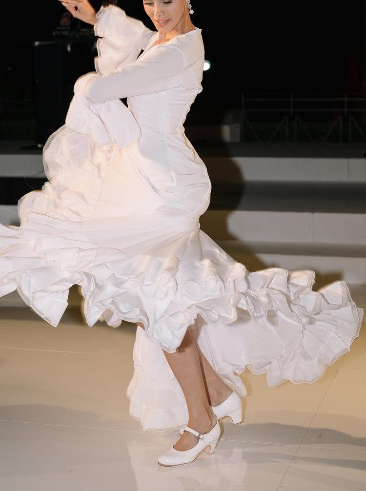 A woman in a white ruffled dress dancing with her skirt swirling in motion.