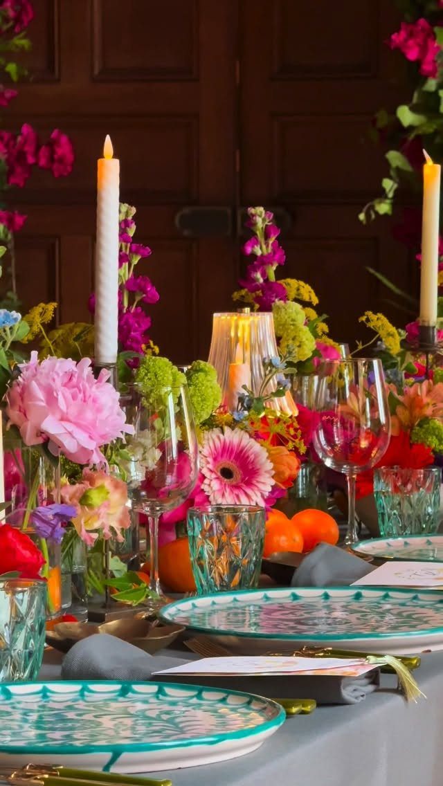 A colorful wedding table decorated with bright flowers, tall candles, and patterned turquoise plates.