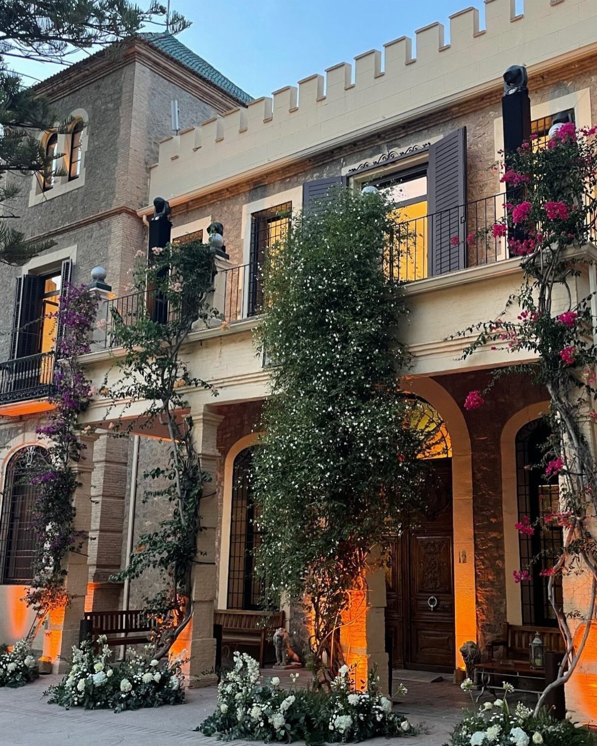 A grand stone villa decorated with climbing vines and white floral arrangements at twilight.