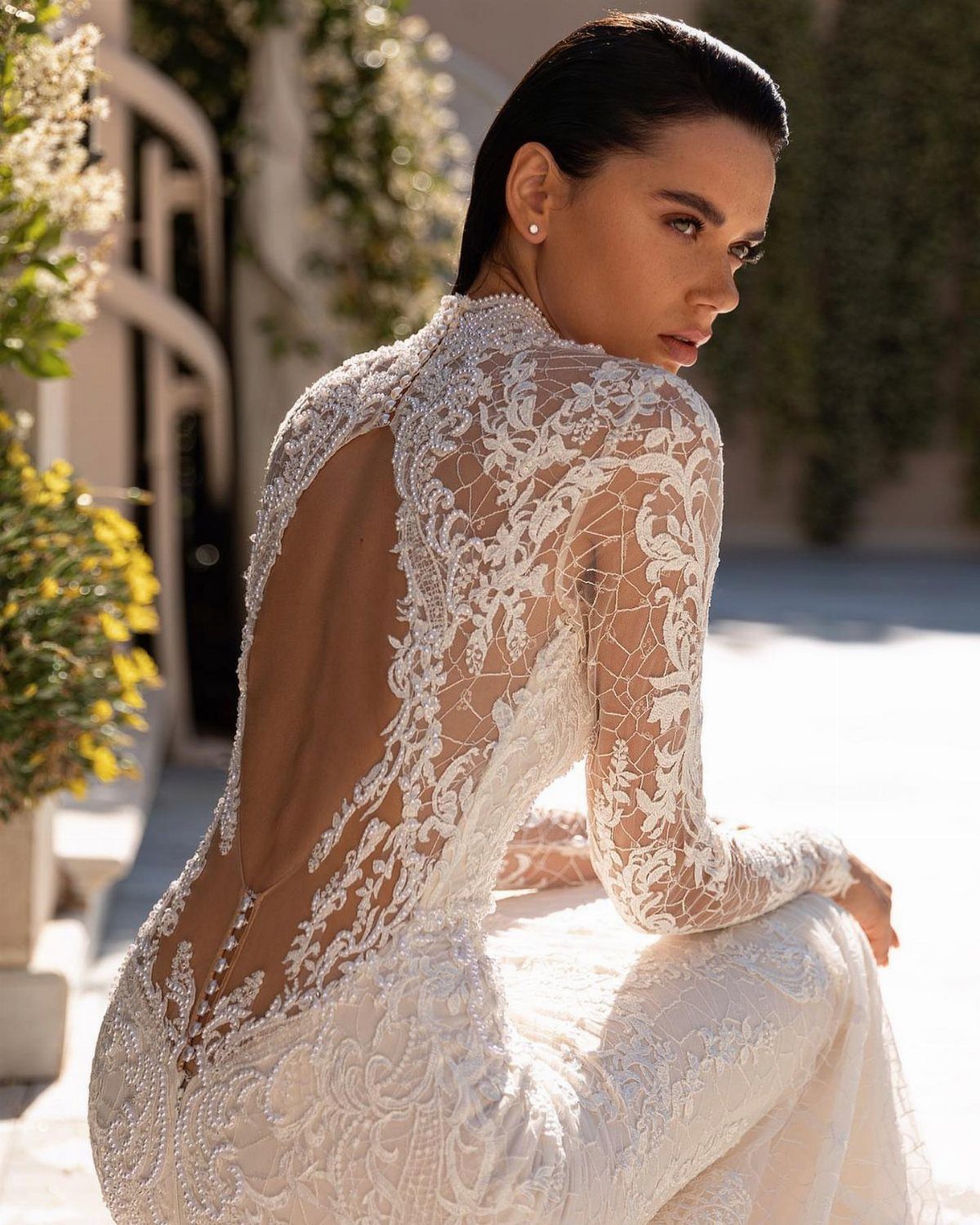 Elegant Mermaid Wedding Dress: 5 Details That Define the Look 3 Woman in a long-sleeved lace wedding dress featuring a large backless design and intricate beadwork.