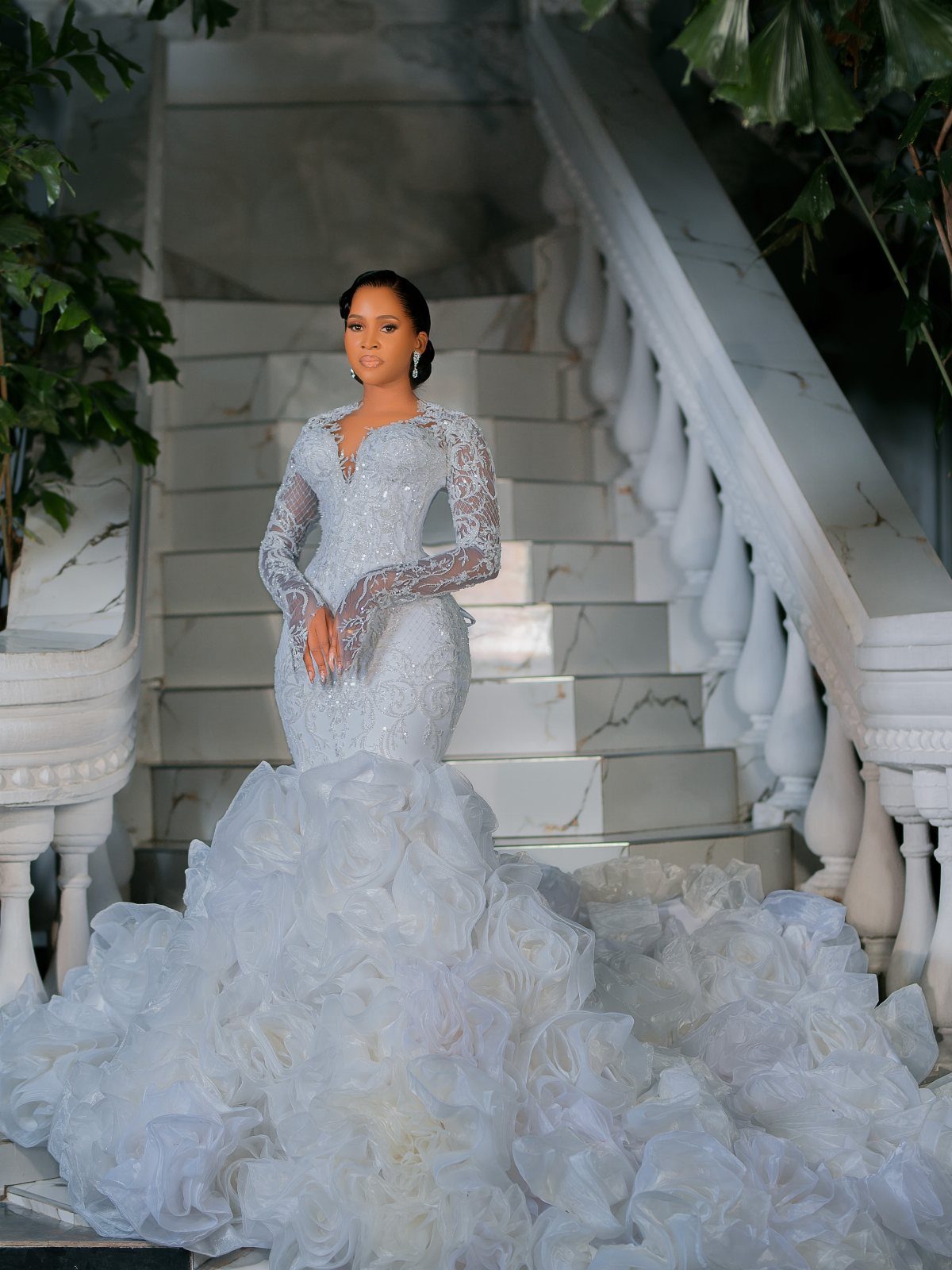 Elegant Mermaid Wedding Dress: 5 Details That Define the Look 1 A woman in a beaded mermaid wedding dress with a large ruffled train on marble stairs.
