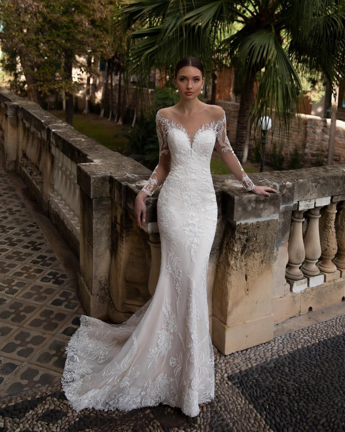 Elegant Mermaid Wedding Dress: 5 Details That Define the Look 5 Woman wearing a white lace mermaid wedding dress standing by a stone balcony outdoors.