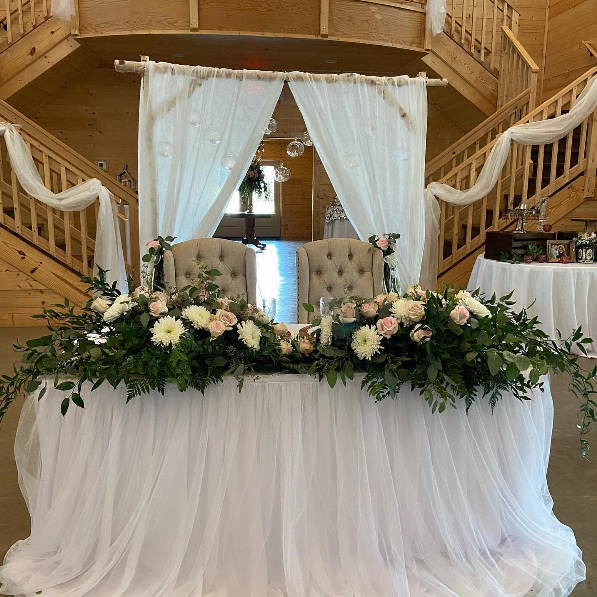 Flowers for Sweetheart Table: 6 Ideas for a Focal Point 1 A wedding sweetheart table decorated with white tulle and a large arrangement of roses and greenery.