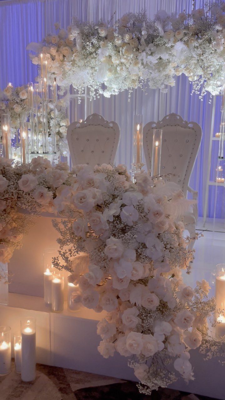 Flowers for Sweetheart Table: 6 Ideas for a Focal Point 3 White floral arrangement cascading down a sweetheart table with lit candles and two elegant chairs.