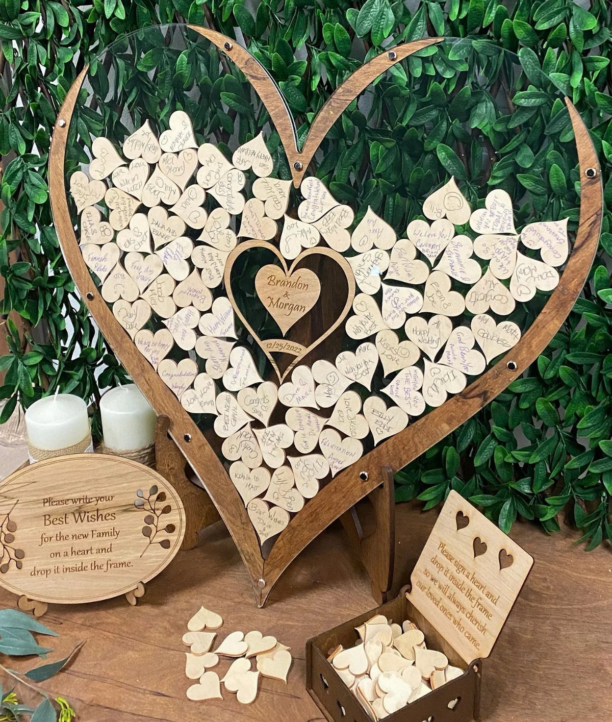 Large wooden heart-shaped frame filled with small wooden hearts on a table with greenery.