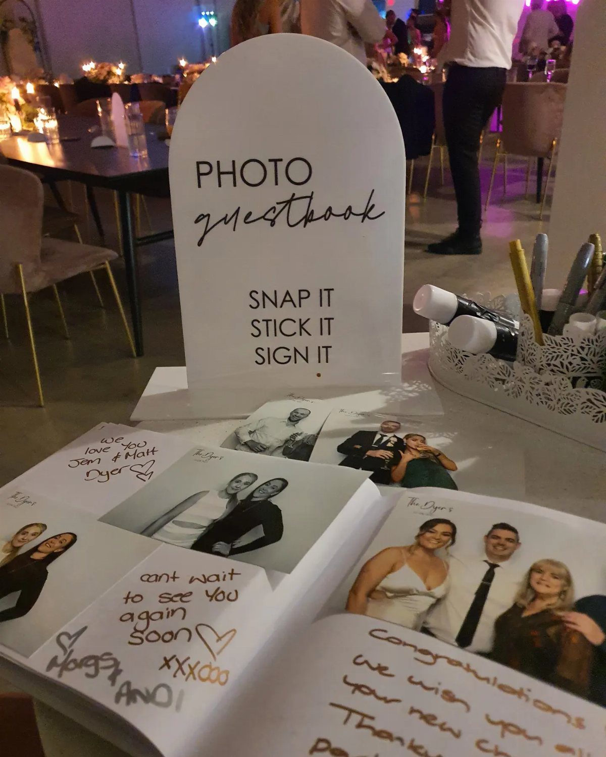 An open photo album guest book with printed pictures and handwritten notes on a table.