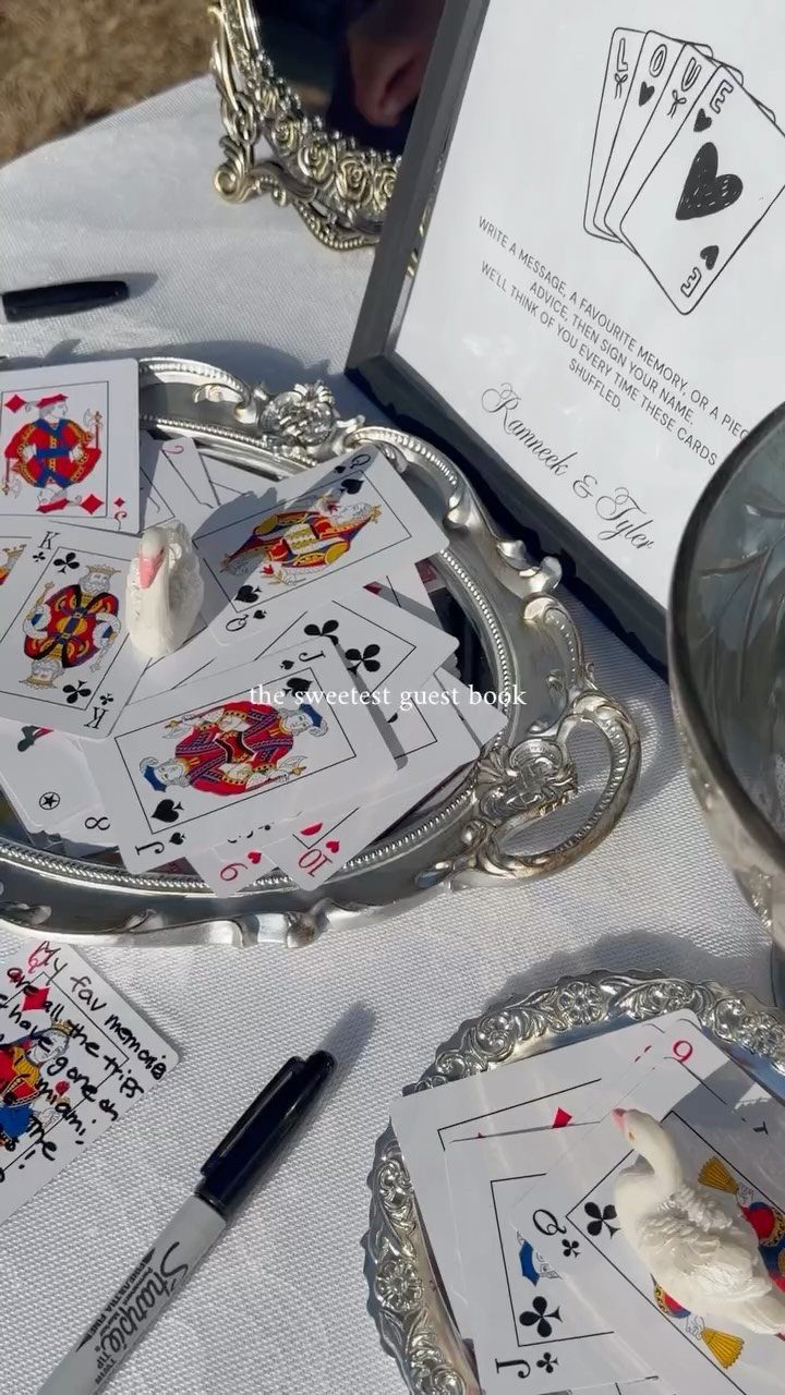 Playing cards scattered on a silver tray and white tablecloth with a black marker.