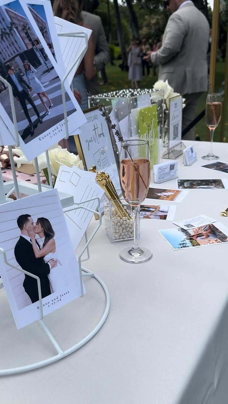 Postcards with wedding photos scattered on a white table next to a glass of rosé wine.