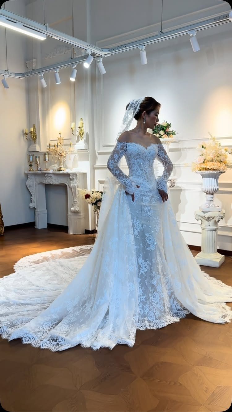 A woman wearing an elegant off-the-shoulder lace wedding dress with a long flowing train.