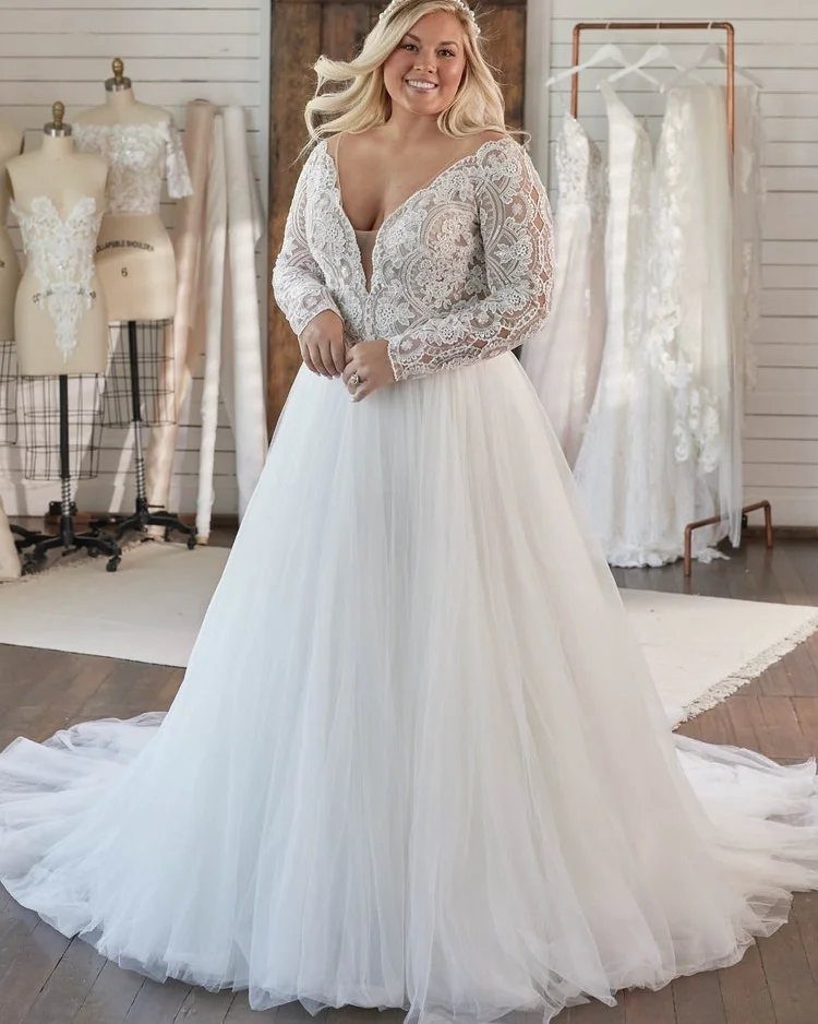 A smiling woman posing in a white lace and tulle wedding dress inside a bridal shop.