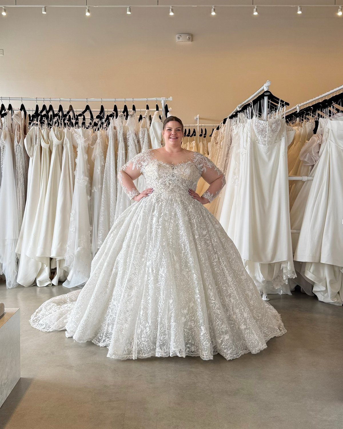 A woman posing in a white lace ballgown wedding dress inside a bridal boutique.